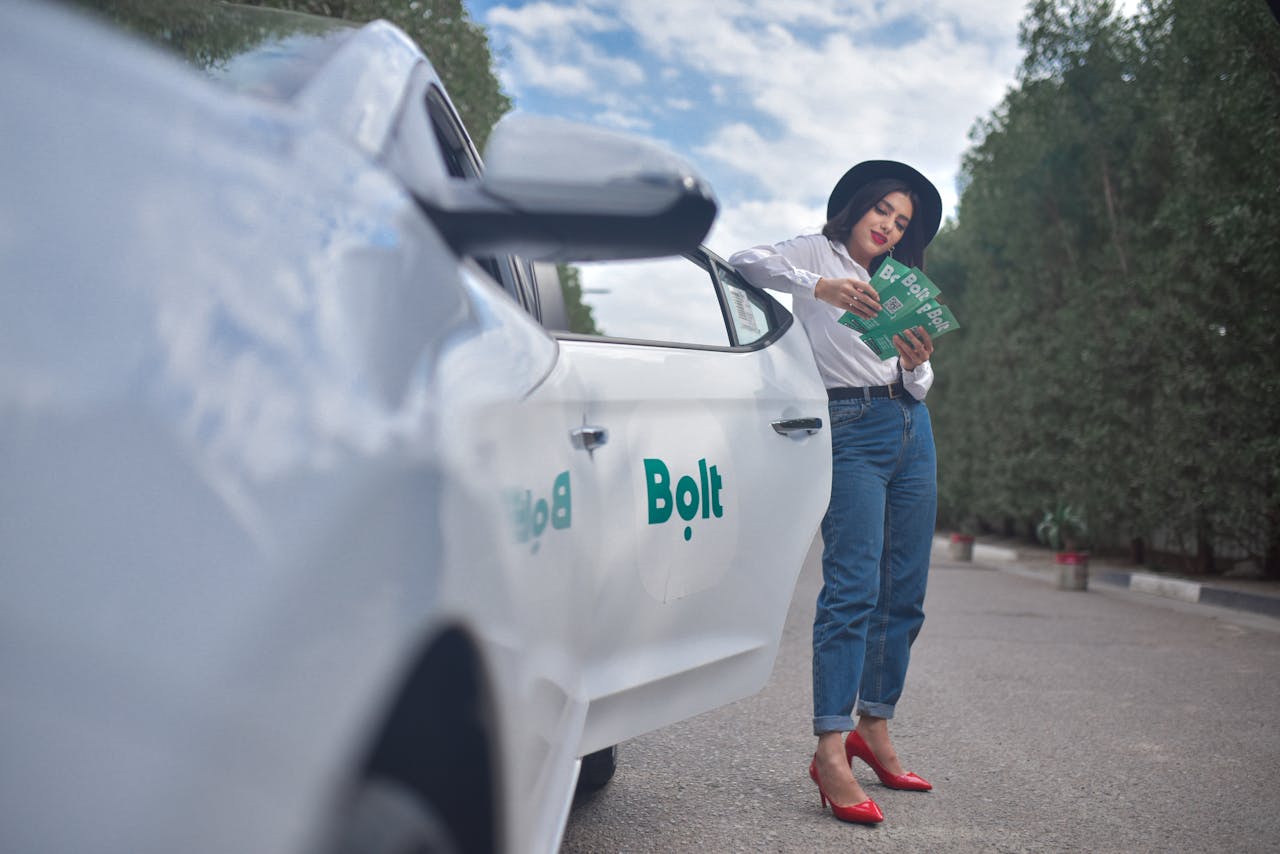 A woman in denim and hat distributing Bolt flyers by a parked car outdoors.