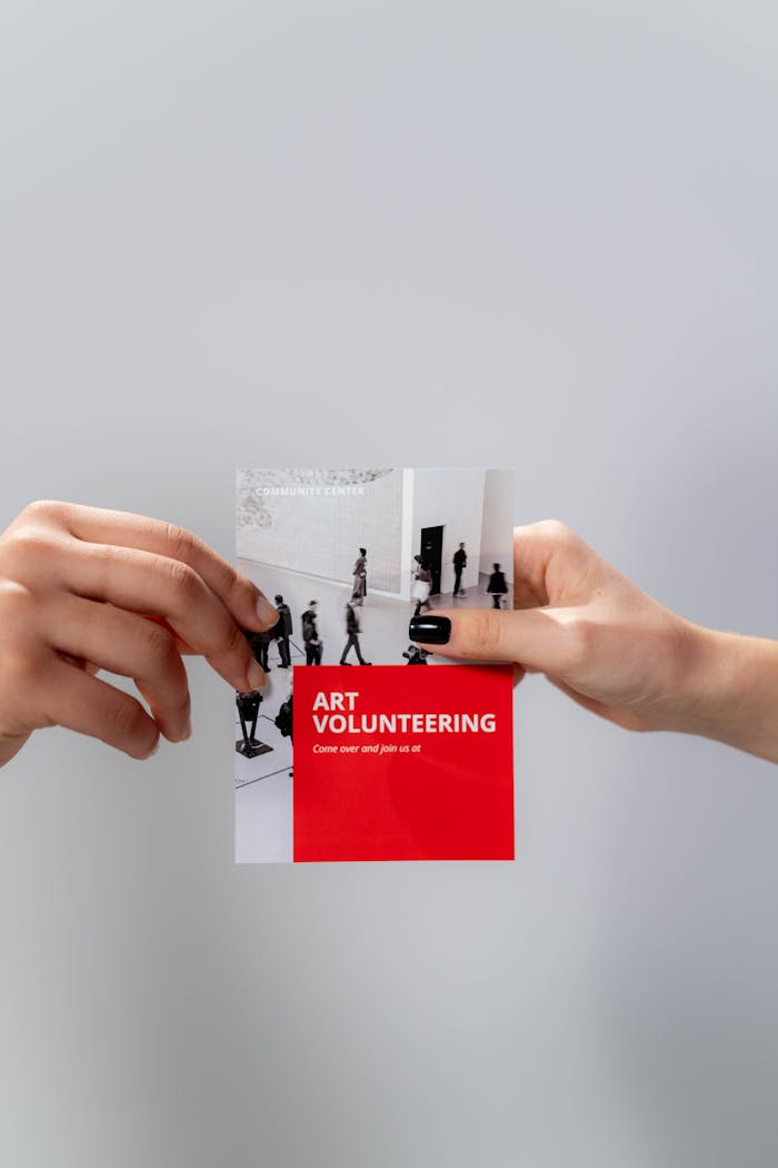 Close-up of hands holding an art volunteering flyer against a neutral background.